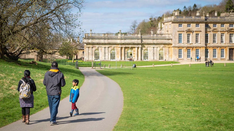Two adults and a child walk down a path towards the house at Dyrham Park, Gloucestershire